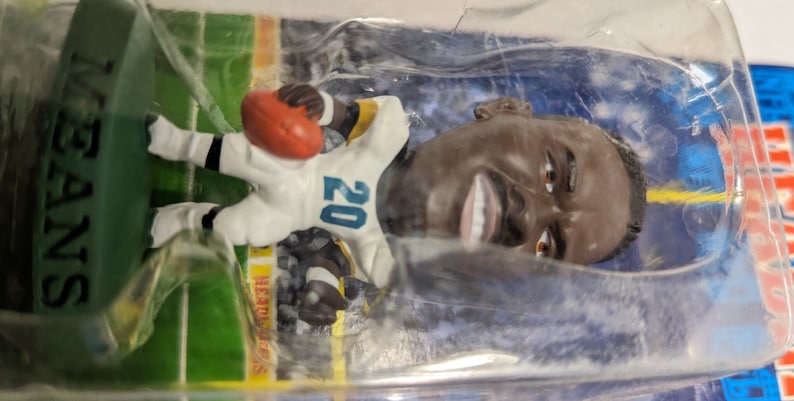 May include: A plastic figurine of a football player wearing a white and teal jersey with the number 20 on it. The player is holding a football and is standing on a green base with the word "SAINTS" printed on it.