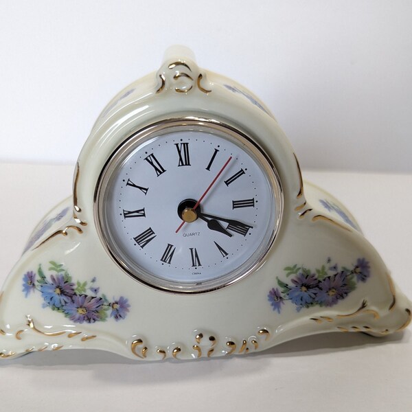 Vintage small porcelain mantle clock, battery operated, adorned in purple and blue daisies with gold trim. Uses N size battery, not included