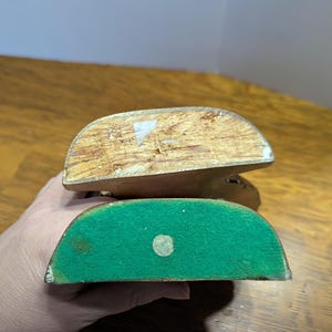 May include: Two wooden bookends, one atop the other, with a curved top and flat bottom. The top bookend is a light brown color, while the bottom bookend has a green felt base. The bookends are likely vintage.