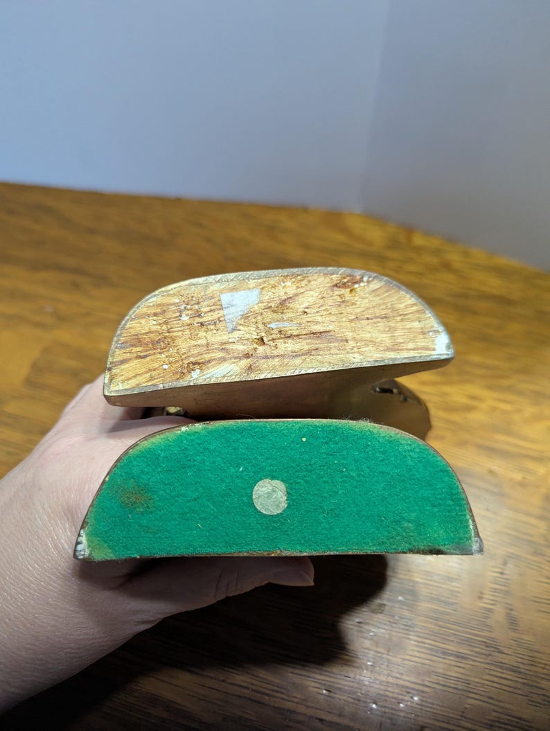 May include: Two wooden bookends, one atop the other, with a curved top and flat bottom. The top bookend is a light brown color, while the bottom bookend has a green felt base. The bookends are likely vintage.
