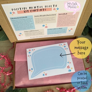 May include: A cardboard box with a pink tissue paper lining. The box contains a self-care kit with a variety of items, including coloring cards, positive thought cards, worry ducks, and a soothing soap and foot mask. The box also includes a blank card with a speech bubble for a personalized message. The text on the box reads "Positive Mental Health Kit Contents".