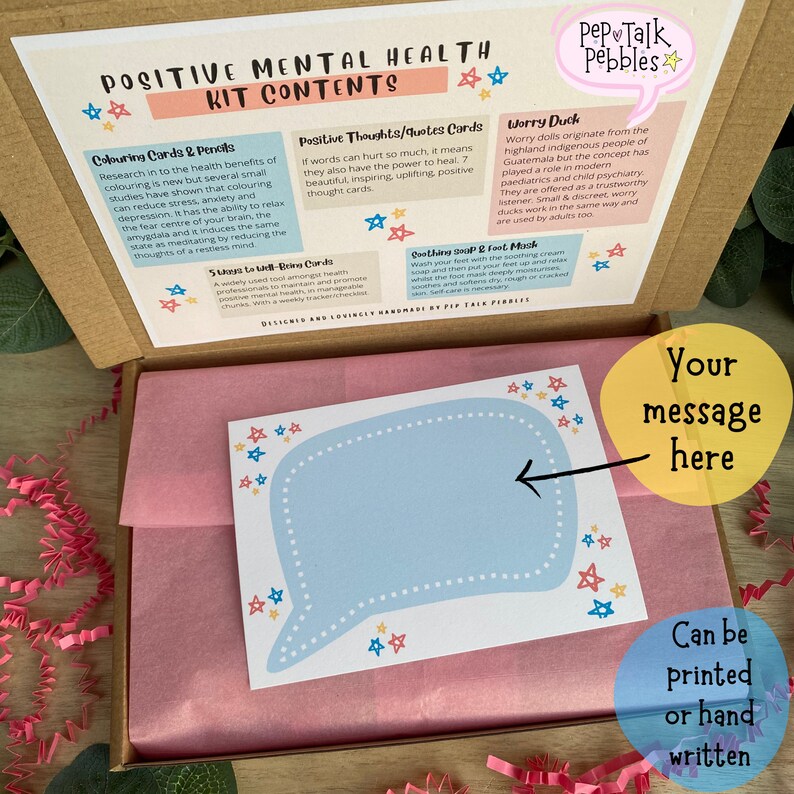 May include: A cardboard box with a pink tissue paper lining. The box contains a self-care kit with a variety of items, including coloring cards, positive thought cards, worry ducks, and a soothing soap and foot mask. The box also includes a blank card with a speech bubble for a personalized message. The text on the box reads "Positive Mental Health Kit Contents".