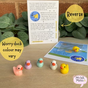 May include: Five small worry ducks in various colors, including pink, purple, blue, white, and yellow. The ducks are sitting on a wooden surface. The text "Worry duck colour may vary" is written in a yellow circle on the left side of the image. The text "Reverse" is written in a yellow circle on the right side of the image. The text "Pep Talk Pebbles" is written in a speech bubble with a star on the bottom right corner of the image.