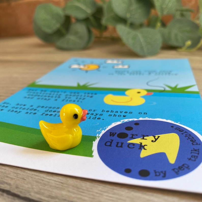 Puede incluir: Un pato de goma amarillo sobre un fondo azul con el texto "worry duck" en un c&iacute;rculo con una flecha amarilla apuntando hacia la derecha. El texto "talk to pep pebbles" est&aacute; debajo del c&iacute;rculo.
