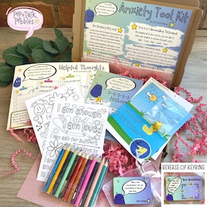 Puede incluir: Una caja de regalo rosa y blanca llena de herramientas para aliviar la ansiedad. La caja incluye p&aacute;ginas para colorear con afirmaciones positivas, un llavero con un ejercicio de respiraci&oacute;n y un juego de l&aacute;pices de colores. La caja est&aacute; etiquetada como "Anxiety Tool Kit" y presenta un personaje de dibujos animados.