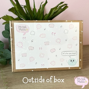 May include: A brown cardboard box with a white label. The label has a pink and white design with speech bubbles and the text "Pep Talk Pebbles". The box is decorated with white polka dots. The text "It's for you hooo!" is written in a speech bubble with a blue cartoon character inside.