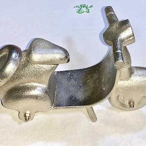 Op de afbeelding: Een zilveren metalen sculptuur van een scooter. De scooter heeft een afgerond lichaam en één wiel aan de achterkant. Het voorwiel is niet zichtbaar op de afbeelding.