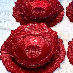 May include: A set of red glass bowls with a textured, ridged design. The bowls are arranged on a white surface. The bowls have a flower-like shape, with a wide, ruffled edge.