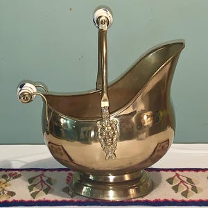 May include: A gold-toned metal ice bucket with a handle and a lion head design. The bucket has a white ceramic handle with blue accents.
