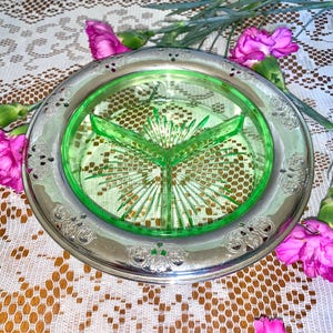 May include: A vintage green glass divided serving dish with a silver rim and ornate design. The dish is sitting on a white lace tablecloth.