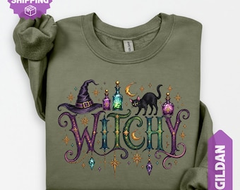 May include: A military green crewneck sweatshirt featuring a graphic print with the word WITCHY in ornate purple and green lettering. The design includes a purple witch hat, a black cat, glowing potion bottles, stars, and a crescent moon.