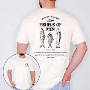 Op de afbeelding: Ivoor kleurig T-shirt met de tekst "JESUS WILL MAKE YOU FISHERS OF MEN" en drie vis illustraties. De achterkant van het shirt bevat ook een Bijbelvers uit Matthe&uuml;s 4:18-19. Een casual kledingstuk.