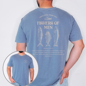 Op de afbeelding: Blauw spijkerstof T-shirt met korte mouwen met een afbeelding op de achterkant met de tekst "FISHERS OF MEN" met drie visillustraties. De tekst "JESUS WILL MAKE YOU" staat boven de afbeelding. Een kleinere afbeelding staat op de voorkant.