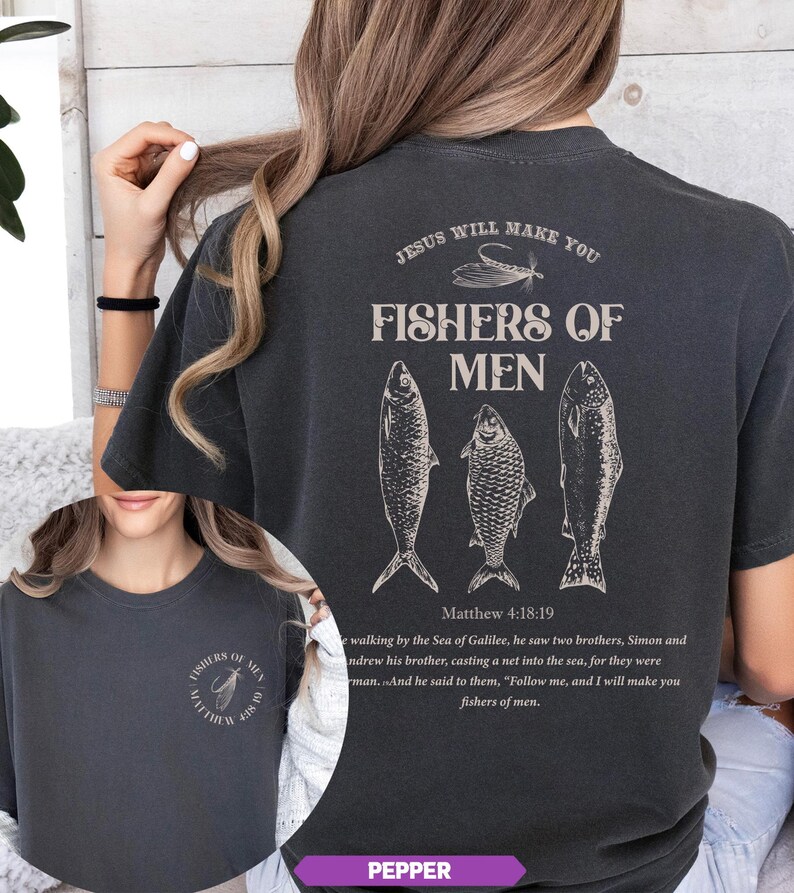 Op de afbeelding: Donkergrijs T-shirt met de tekst "JESUS WILL MAKE YOU FISHERS OF MEN" en drie visillustraties. De tekst "Matthew 4:18:19" staat ook op het shirt. Het shirt heeft de kleur Pepper.