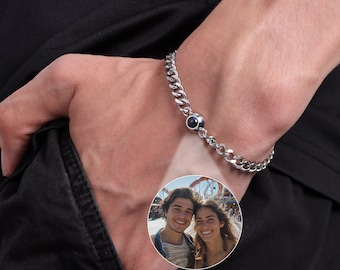 May include: A silver chain bracelet with a black round charm. The charm has a small, clear lens that reveals a photo of a couple.