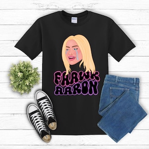 May include: Black t-shirt with a cartoon image of a woman with blonde hair crying. The text "Fawk Aaron" is written in pink and black letters.