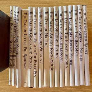 May include: A collection of fifteen hardcover books with cream-coloured spines, each featuring black printed titles including The Tale of Peter Rabbit, The Tale of Squirrel Nutkin, The Tale of Two Bad Mice, Mr. Jeremy Fisher, and other classic stories.