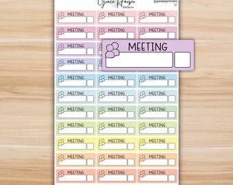May include: A sticker sheet featuring rows of rectangular labels in various pastel colors. Each label displays the text MEETING, a small icon of three people, and a blank white box for notes. A single larger purple sticker is overlaid on the sheet.