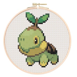May include: A cross-stitch pattern of a green and brown Pokemon character with a leafy sprout on its head. The character is in a round wooden embroidery hoop.