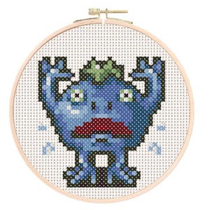 May include: A blue monster with a green leafy head is depicted in a cross-stitch pattern. The monster has large eyes, a red mouth, and is raising its arms in the air. The monster is stitched on white fabric and framed in a wooden hoop.