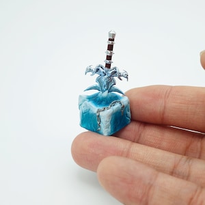 May include: A miniature blue ice block with a silver and red sword frozen inside. The sword has a skull-like design and is surrounded by a silver chain.