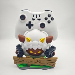 May include: A white sheep character with brown ears and horns, holding two black guns, is standing on a wooden platform. The sheep is wearing a white controller with black buttons and a black joystick. The controller has the words "Turbo, Home, Clear, Select, Start, 1, 2, 3, 4, X, Y, A, B" printed on it.