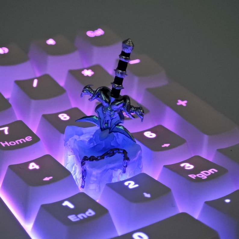 May include: A silver and black sword figurine with a blue and white base, sitting on a white keyboard with purple backlighting. The keyboard has keys labeled with numbers and letters.