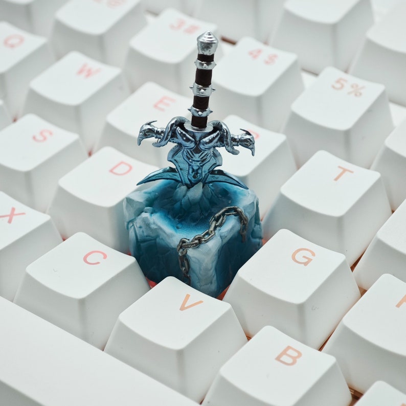 May include: A blue and silver sword figurine on a white keyboard. The sword is frozen in a block of ice with a chain wrapped around it.