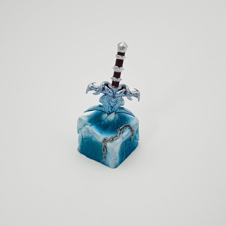 May include: A blue and silver miniature sword with a red handle, mounted on a blue and white ice-themed base. The sword is surrounded by a silver chain.