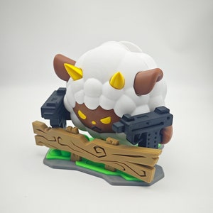 May include: A white sheep with brown ears and horns, holding two black guns, standing on a wooden fence with green grass.
