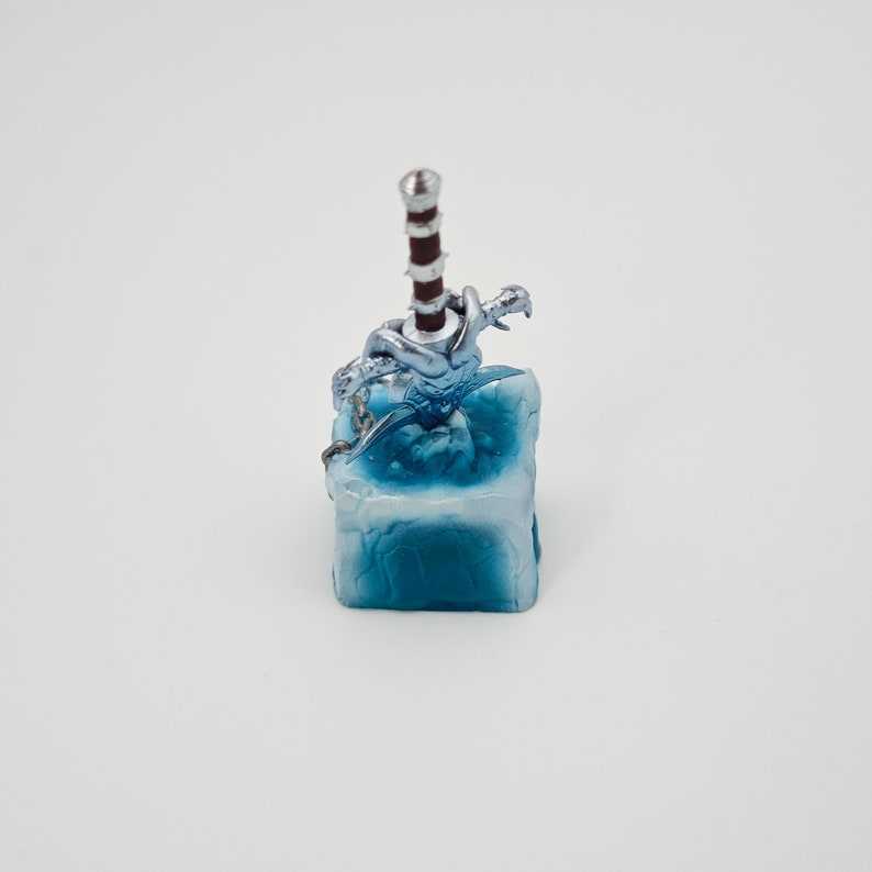 May include: A silver and red sword with a dragon design is frozen in a blue ice cube. The cube is made of resin and has a textured surface.