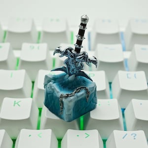 May include: A blue and silver miniature sword on a blue and white ice-themed keyboard keycap.