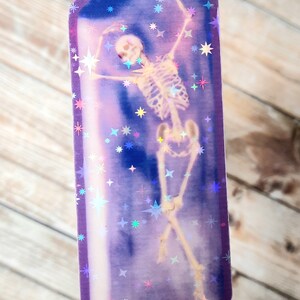 May include: A purple crystal-shaped sticker with a holographic finish features a skeleton dancing inside. The background is filled with iridescent stars.
