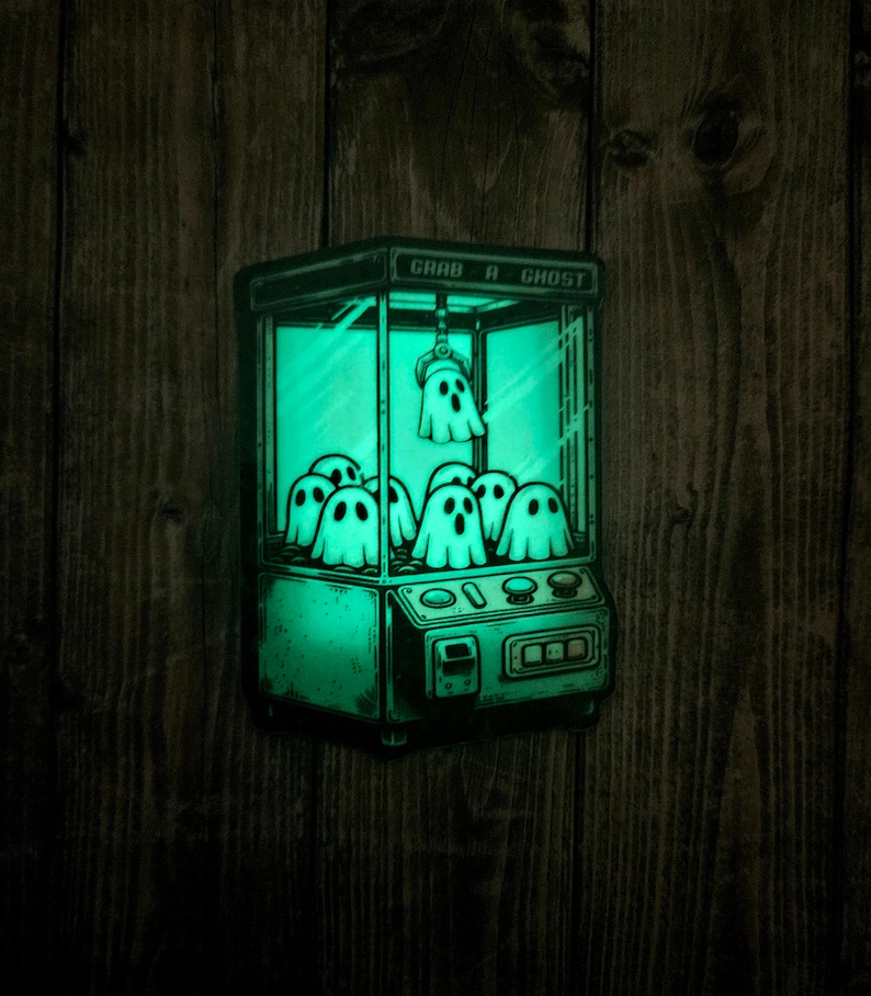 May include: A green glow-in-the-dark sticker of a vintage claw machine with the text "Grab a Ghost" on the front. The claw machine is filled with cartoon ghosts.