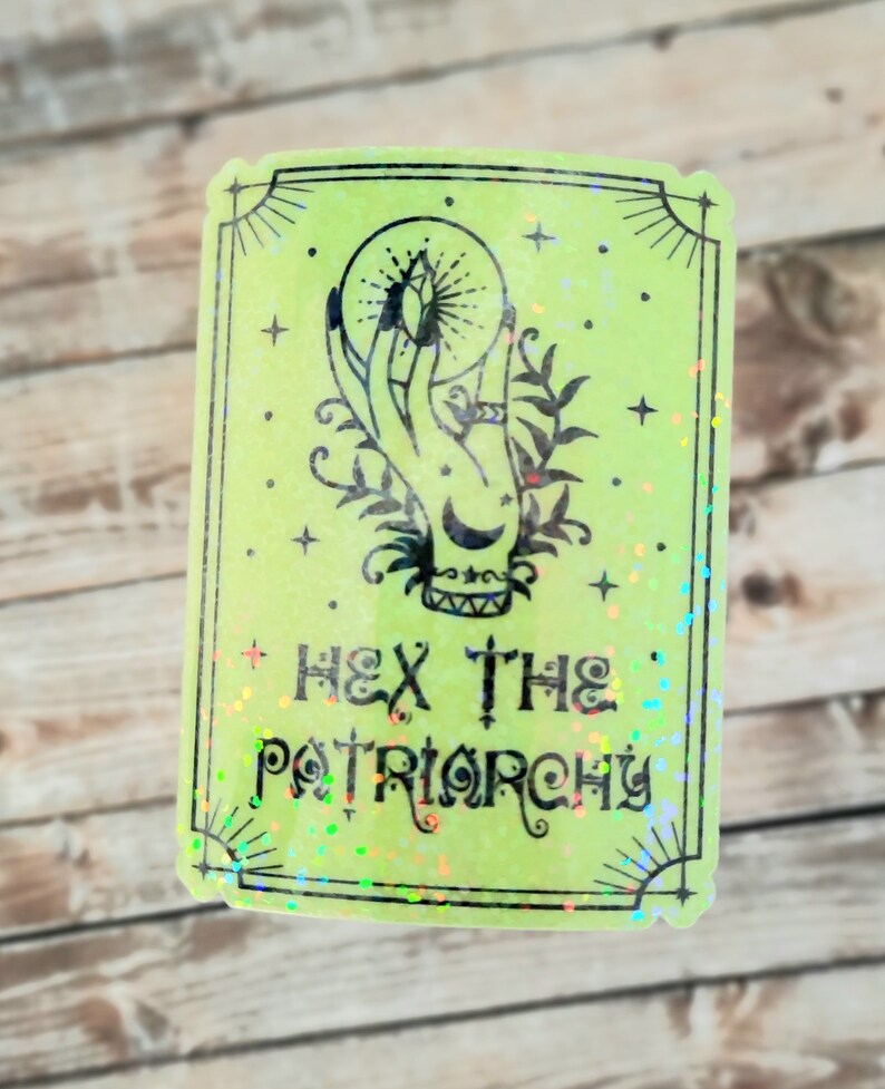 May include: A green holographic sticker with a black illustration of a hand holding a crystal ball. The text "HEX THE PATRIARCHY" is written below the illustration.