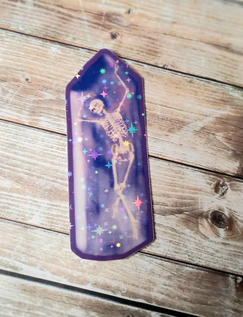May include: A holographic sticker of a skeleton dancing inside a purple crystal with a glittery background.