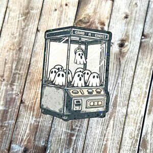 May include: A vintage-style claw machine with the text "Grab A Ghost" on the front. The machine is filled with cartoon ghosts.