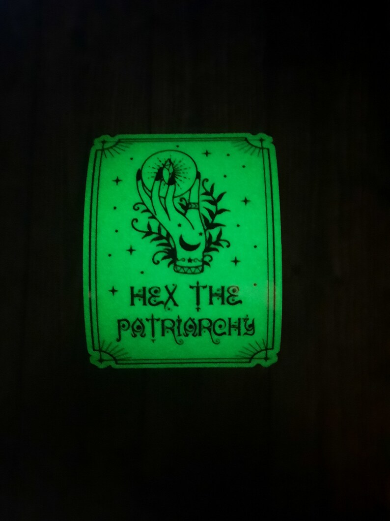 May include: A green glow-in-the-dark sticker with a black and white illustration of a hand holding a crystal ball. The text "HEX THE PATRIARCHY" is written below the illustration.