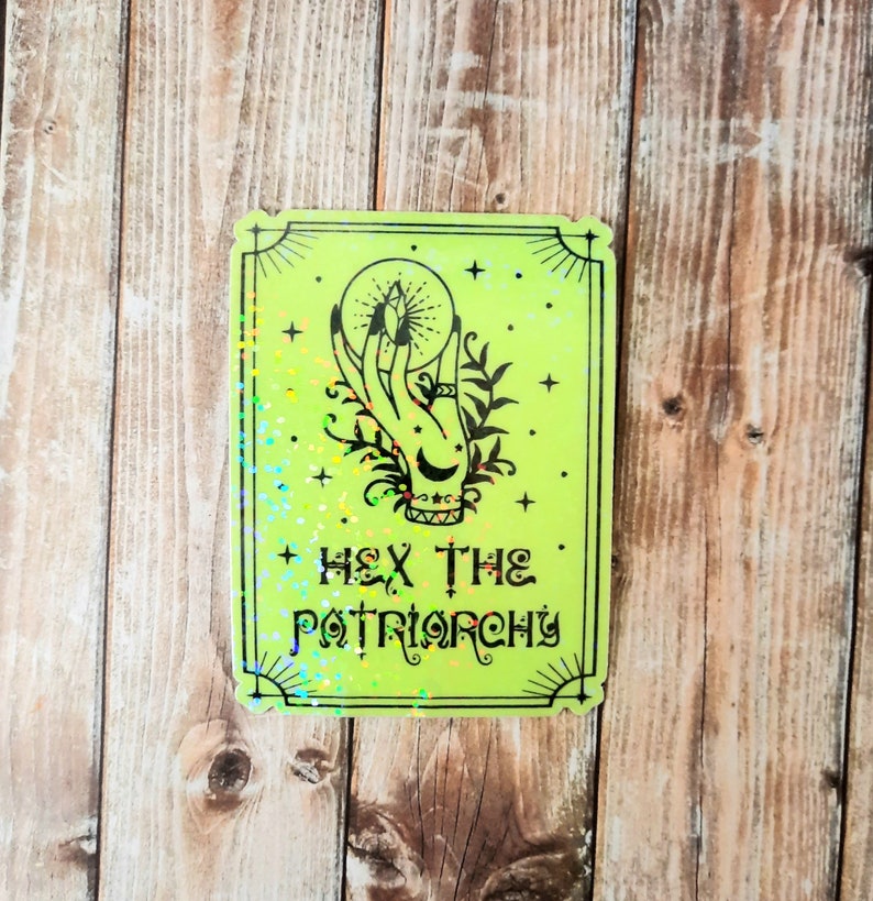 May include: A green holographic sticker with a black illustration of a hand holding a crystal orb. The text "HEX THE PATRIARCHY" is printed below the illustration.