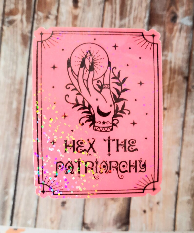 May include: Pink sticker with a black and white illustration of a hand holding a crystal ball. The text "HEX THE PATRIARCHY" is printed below the illustration.