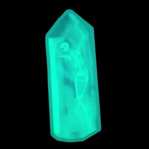 May include: A turquoise blue crystal-shaped object with a skeleton inside. The skeleton is posed with arms raised and legs crossed.