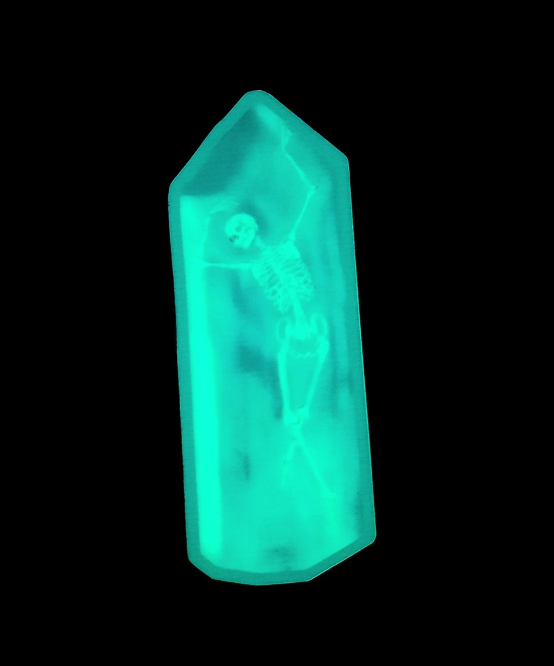 May include: A turquoise blue crystal-shaped object with a skeleton inside. The skeleton is posed with arms raised and legs crossed.