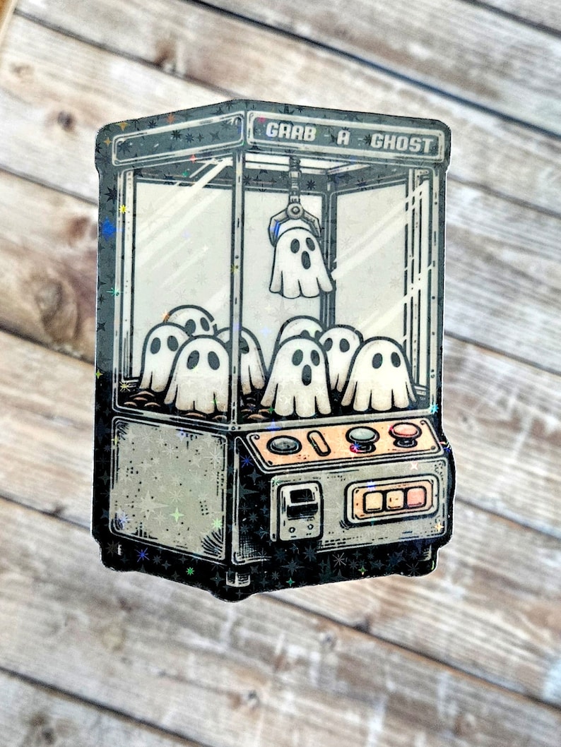 May include: A vintage-style claw machine with the text "Grab A Ghost" on the top. The machine is filled with white ghosts. The claw is holding a ghost.