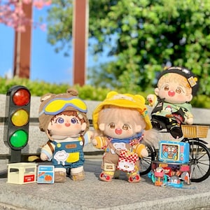 May include: Three plush toys, each with a different design and outfit. The first toy is a brown bear wearing a blue and white jumpsuit and a yellow aviator hat with goggles. The second toy is a yellow bear wearing a brown and yellow jumpsuit with a yellow hat and a brown bear patch. The third toy is a white bear wearing a green and black shirt with a penguin design and a yellow hat. The toys are sitting on a table with a traffic light, a toy box, and a toy wagon.