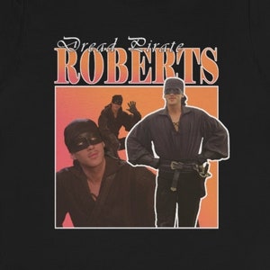 May include: Black t-shirt with a vintage-style graphic of a man in a pirate costume. The graphic has the text "Dread Pirate Roberts" in orange and white.