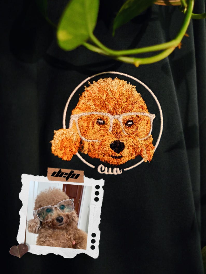 Puede incluir: Una camiseta negra con una imagen bordada de un perro con gafas. El perro es marr&oacute;n y tiene el nombre "Cua" bordado debajo. Una foto de un perro similar con gafas est&aacute; en la esquina inferior izquierda de la imagen.