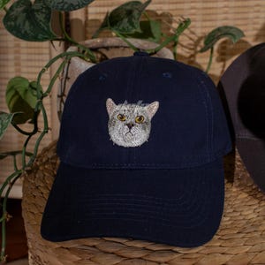 Puede incluir: Gorra de b&eacute;isbol azul marino con un bordado de la cara de un gato. La gorra tiene una visera curva y la palabra "defo" est&aacute; impresa en blanco. Un accesorio de moda.