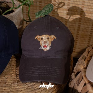 May include: Two baseball caps, one black with an embroidered image of a brown dog, and one beige.