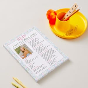 K&ouml;nnte beinhalten: Ein Lebenslauf mit dem Namen "Riley Summer Hanson" und einem Foto wird auf einer wei&szlig;en Oberfl&auml;che angezeigt. Ein gelber Schreibtisch-Organizer enth&auml;lt ein Lineal, einen Bleistift und B&uuml;roklammern. Ein gelber Stift und ein Textmarker sind ebenfalls vorhanden.