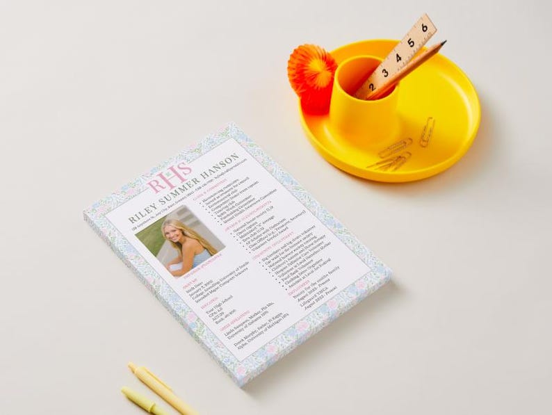 K&ouml;nnte beinhalten: Ein Lebenslauf mit dem Namen "Riley Summer Hanson" und einem Foto wird auf einer wei&szlig;en Oberfl&auml;che angezeigt. Ein gelber Schreibtisch-Organizer enth&auml;lt ein Lineal, einen Bleistift und B&uuml;roklammern. Ein gelber Stift und ein Textmarker sind ebenfalls vorhanden.